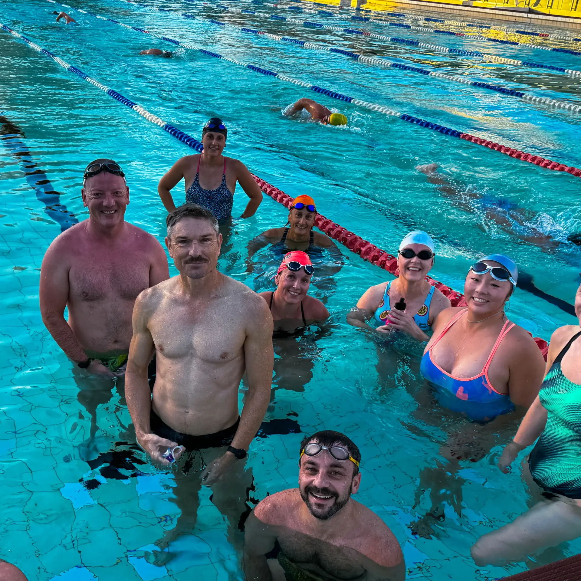 Group of adults enjoying Mornign Squad Sessions together in Sydney pool, wearing swim caps and goggles.
